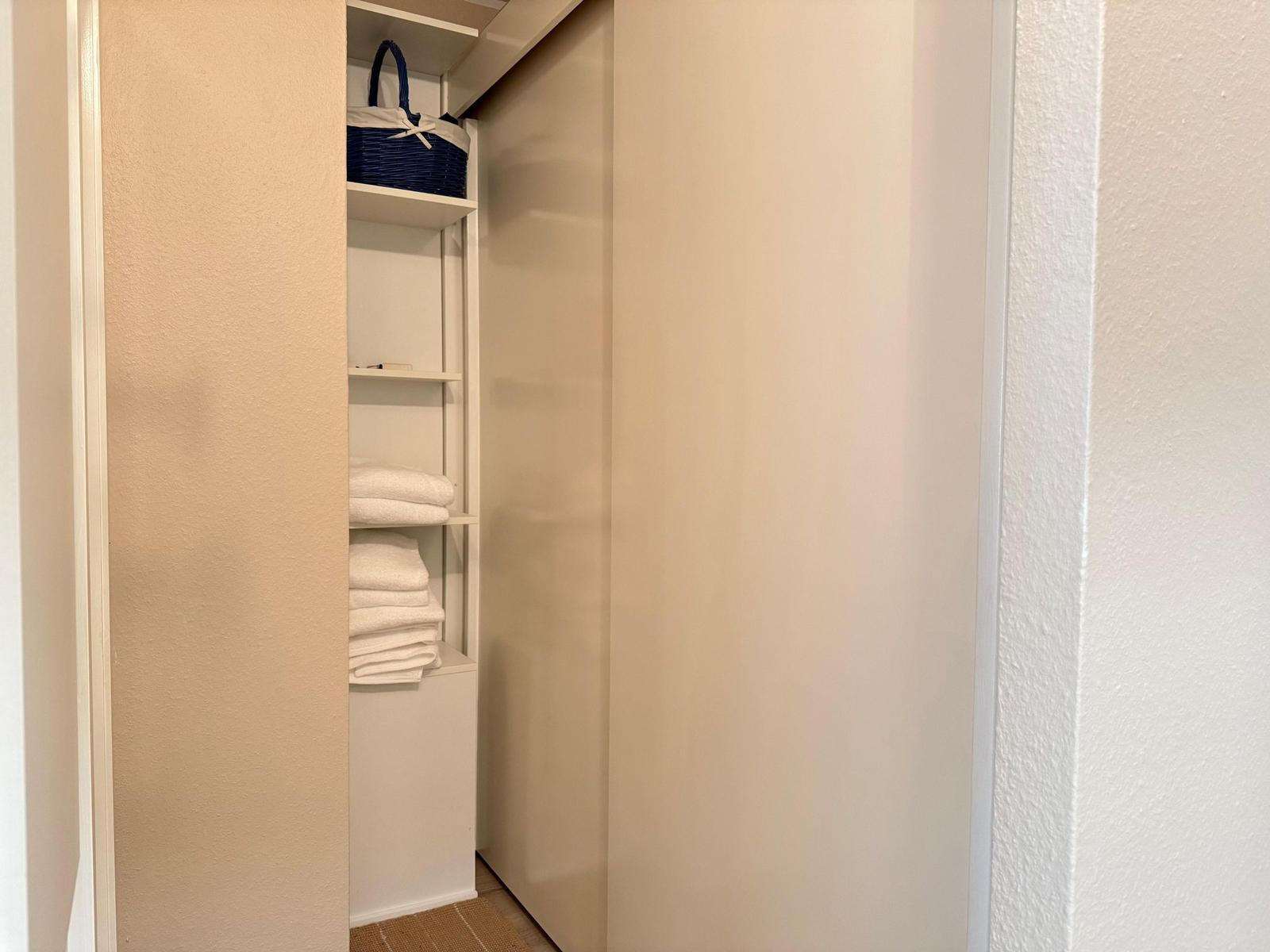 Schrank mit offenen Regalen, darin Handtuchstapel und blauer Korb.