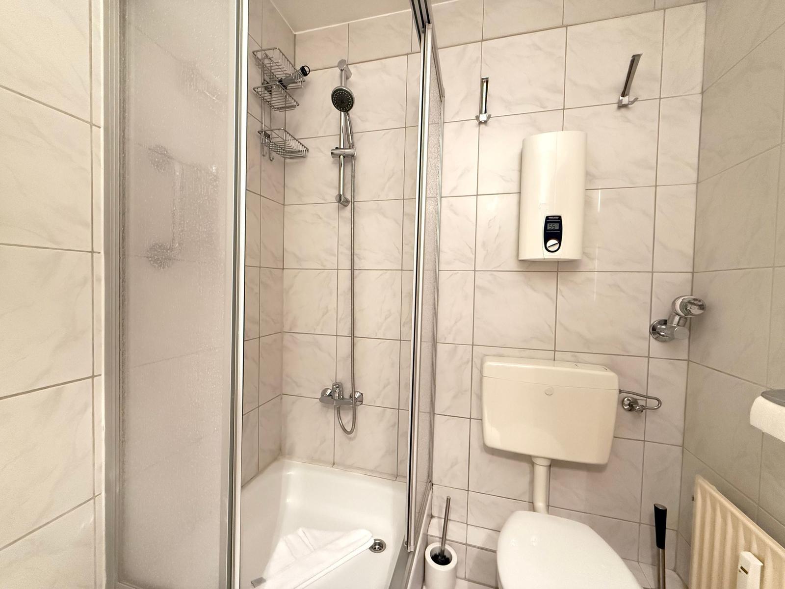 Dusche mit Duschbrause, Toilette und Heizkörper an der Wand.