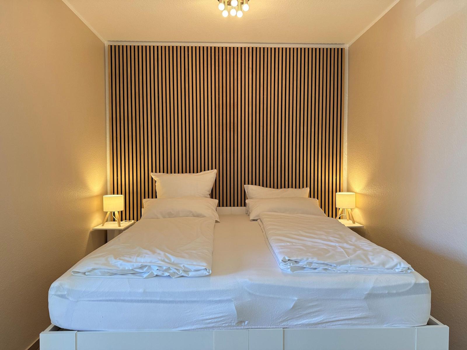 Schlafzimmer mit Doppelbett, Holzpaneelen an der Wand und zwei Nachttischen mit Lampen.