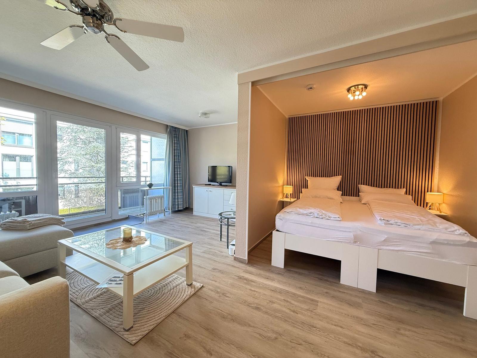 Ein Schlafzimmer mit Doppelbett und Wohnbereich mit Glas-Tisch und Balkon.