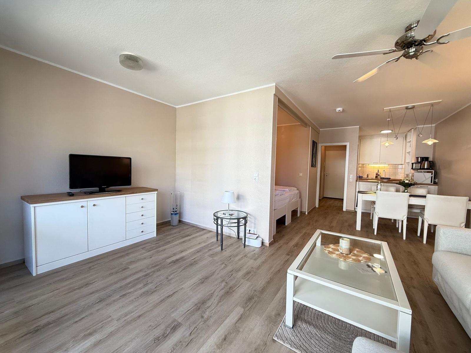 Wohnung mit Wohn- und Essbereich, Küche und Schlafzimmer. Holzfußboden und weiße Möbel.