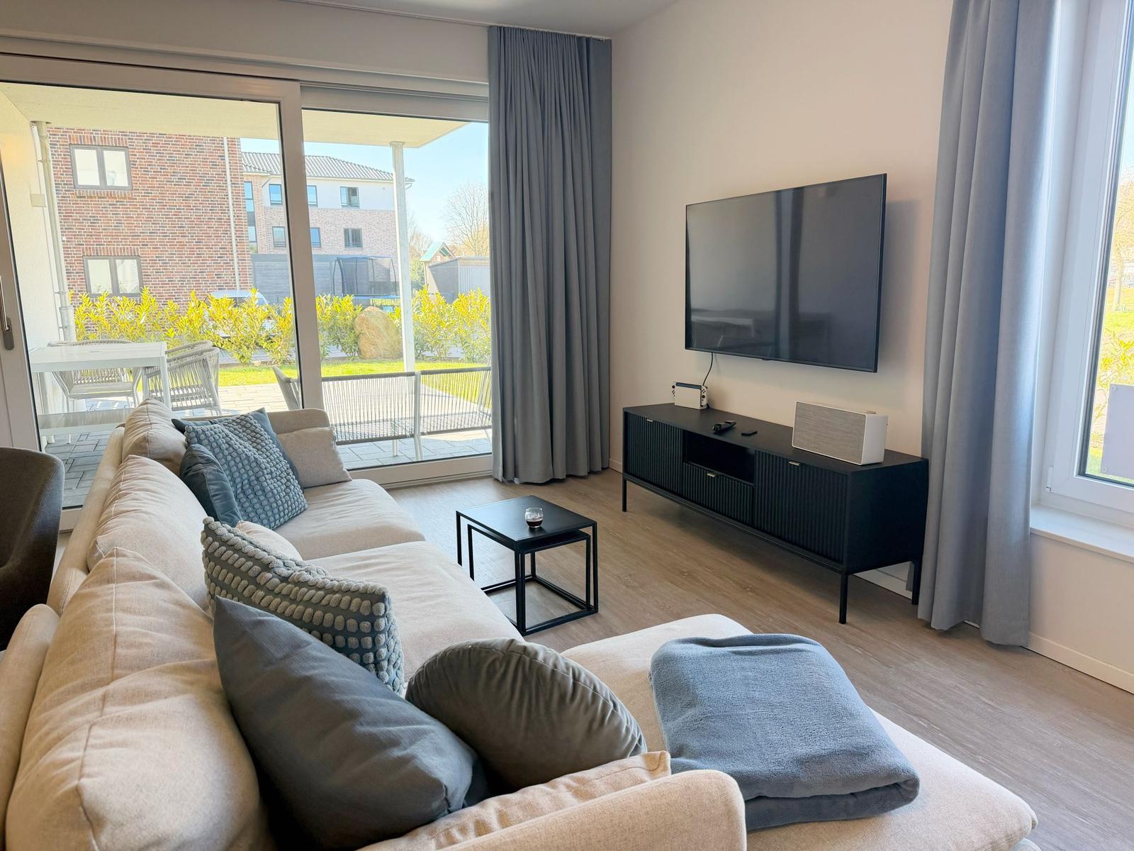 Wohnzimmer mit Sofa, Fernseher und Blick auf Balkon.