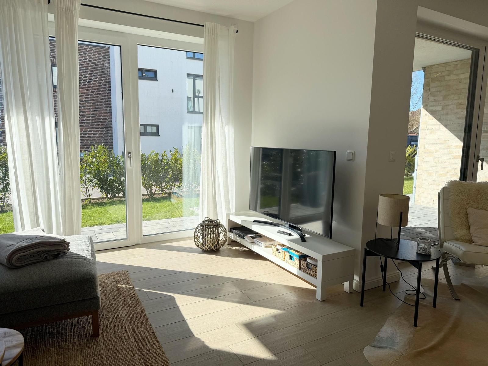 Wohnzimmer mit Fernseher, Glasfront und Sitzgelegenheiten.