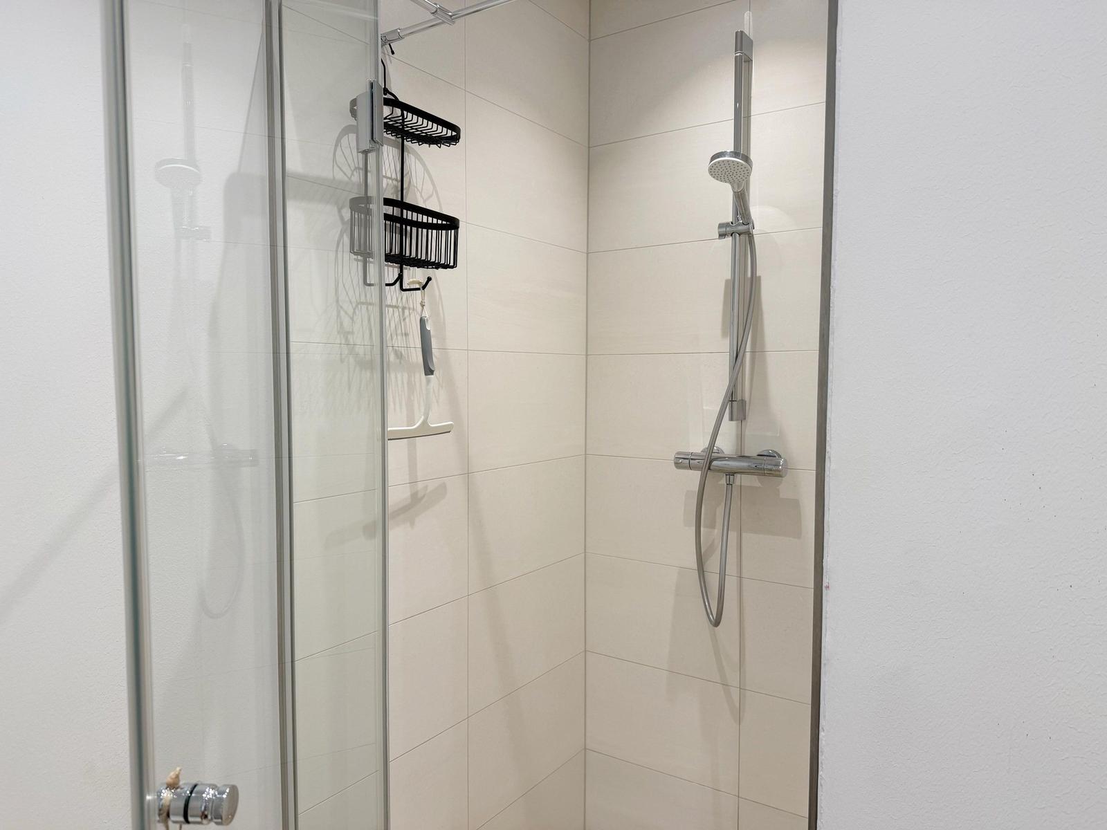 Duschkabine mit Glaswand, Duschbrause und schwarzen Aufhängern an der Wand.