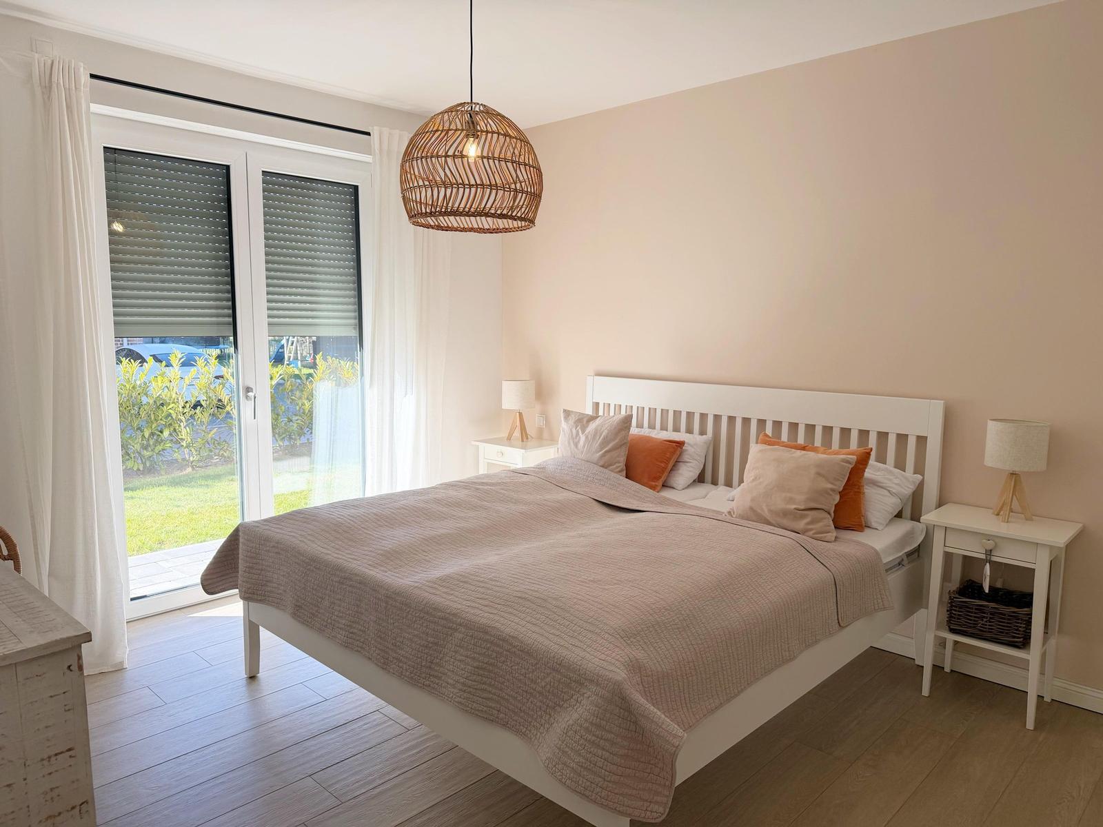 Schlafzimmer mit Bett, Nachttischen und Fenster zur Terrasse.