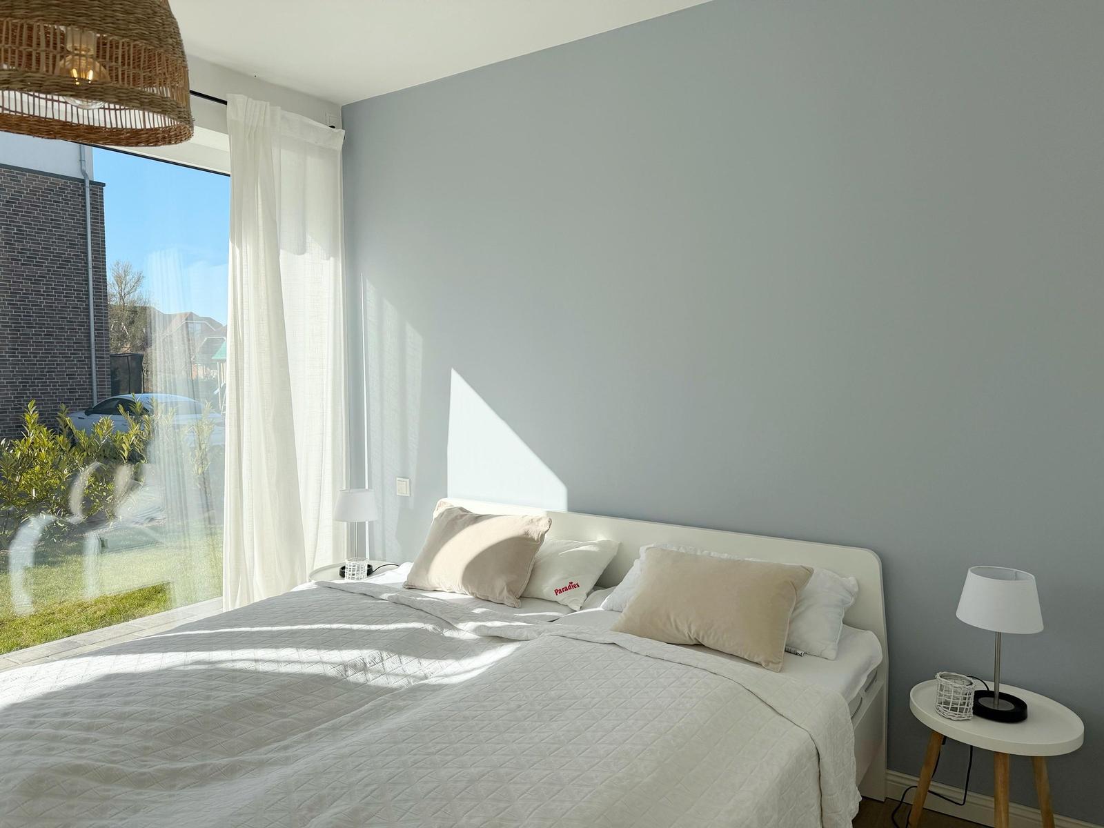 Schlafzimmer mit Bett, Nachttisch und Fenster mit Blick auf Garten.