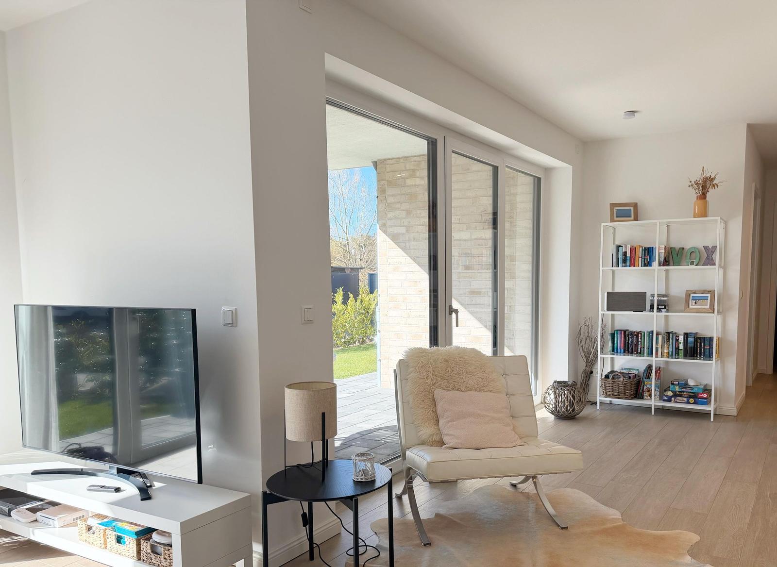 Wohnzimmer mit TV, Sessel und Bücherregal. Durchgang zur Terrasse.