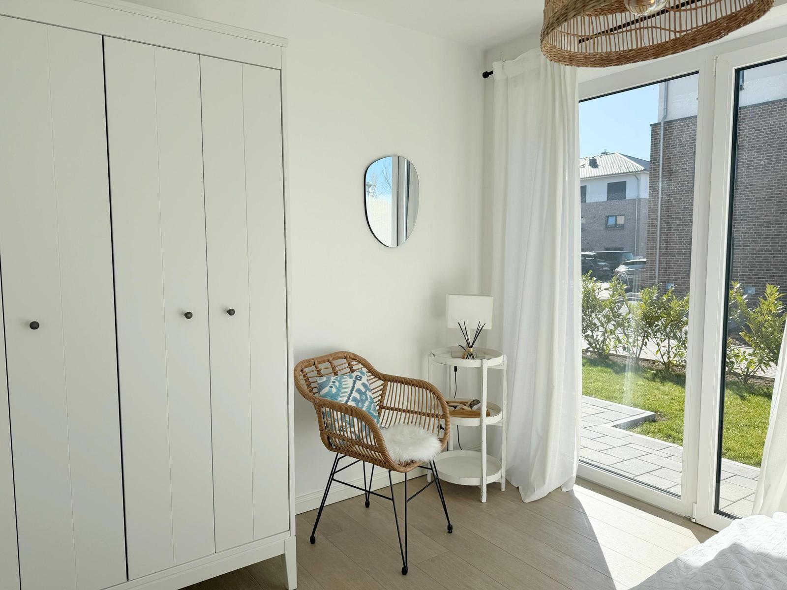 Schlafzimmer mit weißem Schrank, Rattan-Stuhl und Blick auf Balkon.