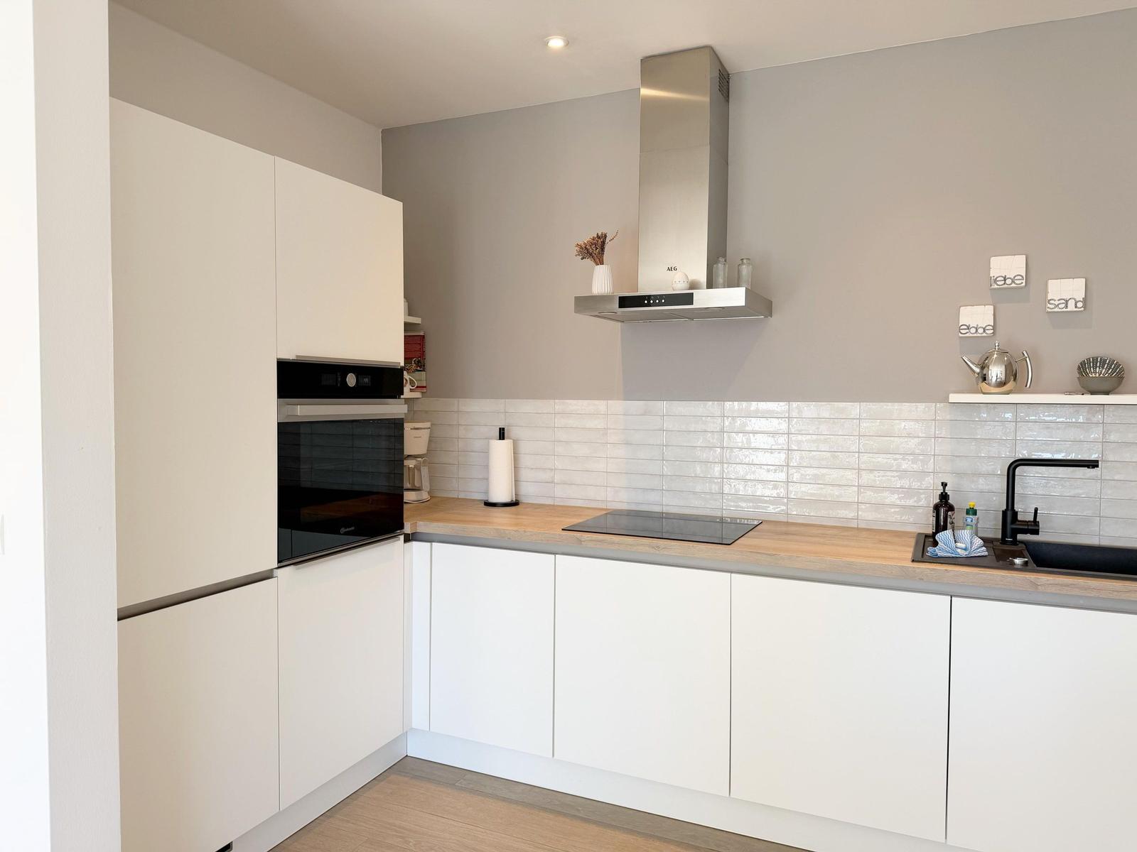 Moderne Küche mit weißen Schränken, Holzoberfläche und Edelstahl-Abluftkamin.
