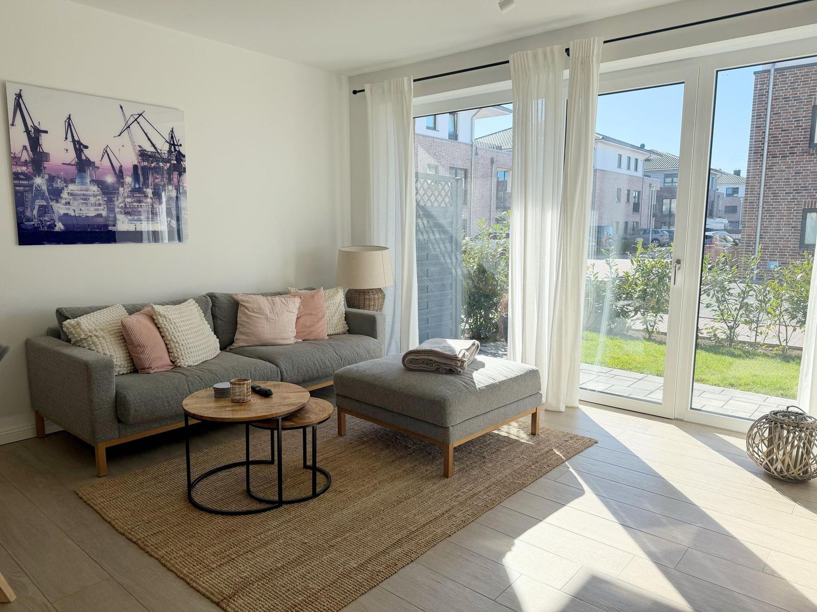 Wohnzimmer mit Sofa, Beistelltisch und Sitzbank. Große Fenster mit Blick auf Garten.