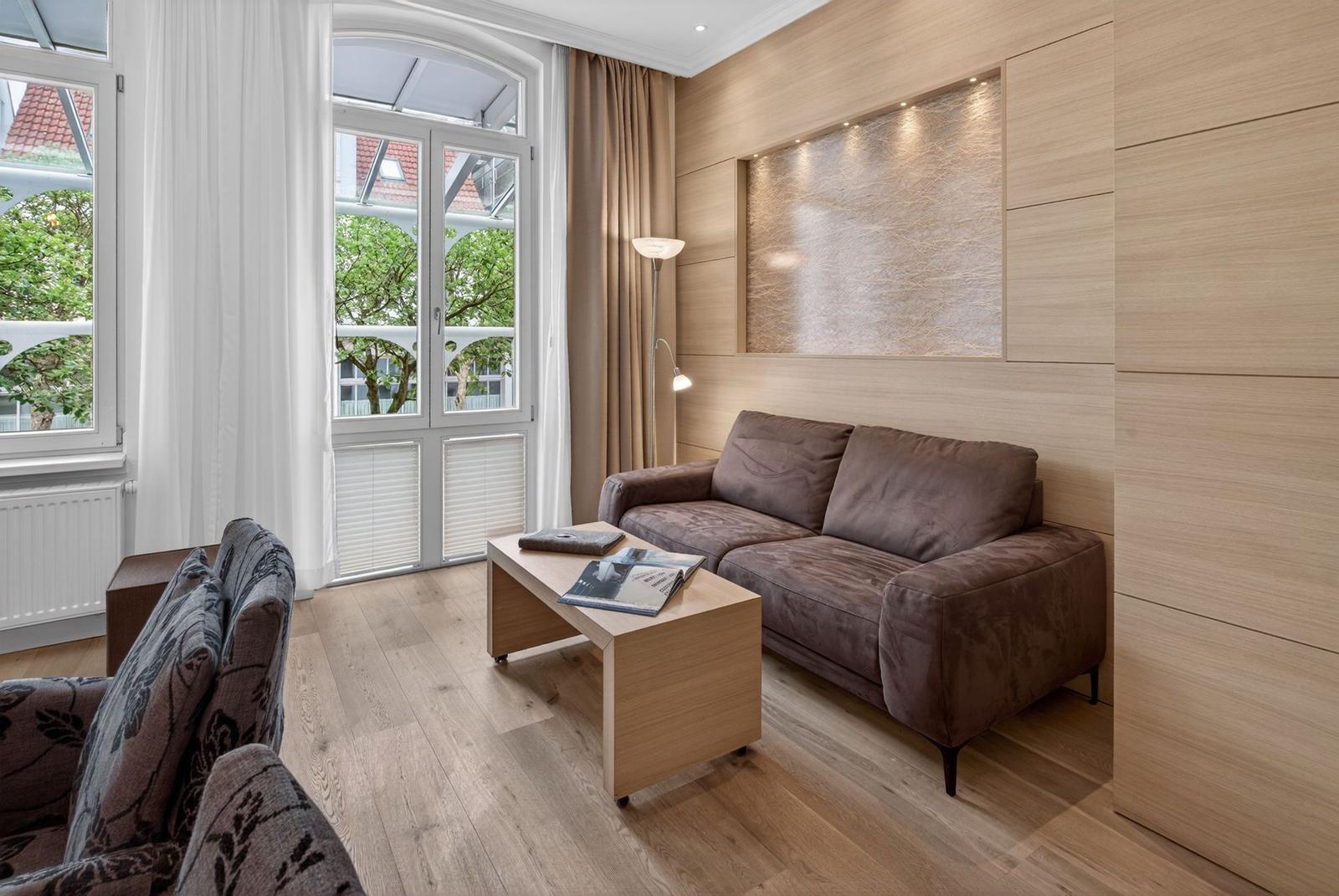 Wohnzimmer mit braunem Sofa, Holzmöbeln und Fenster mit Blick auf Balkon.