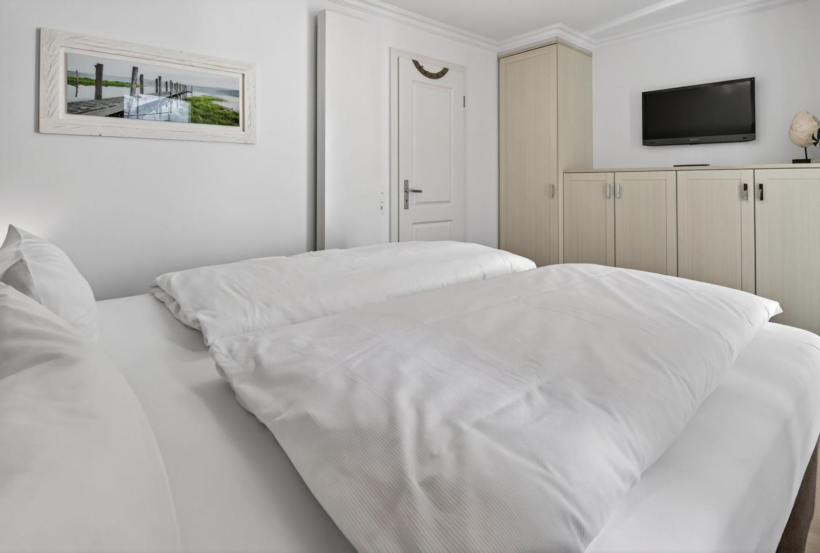 Schlafzimmer mit Doppelbett, Kleiderschrank und Fernseher an der Wand.