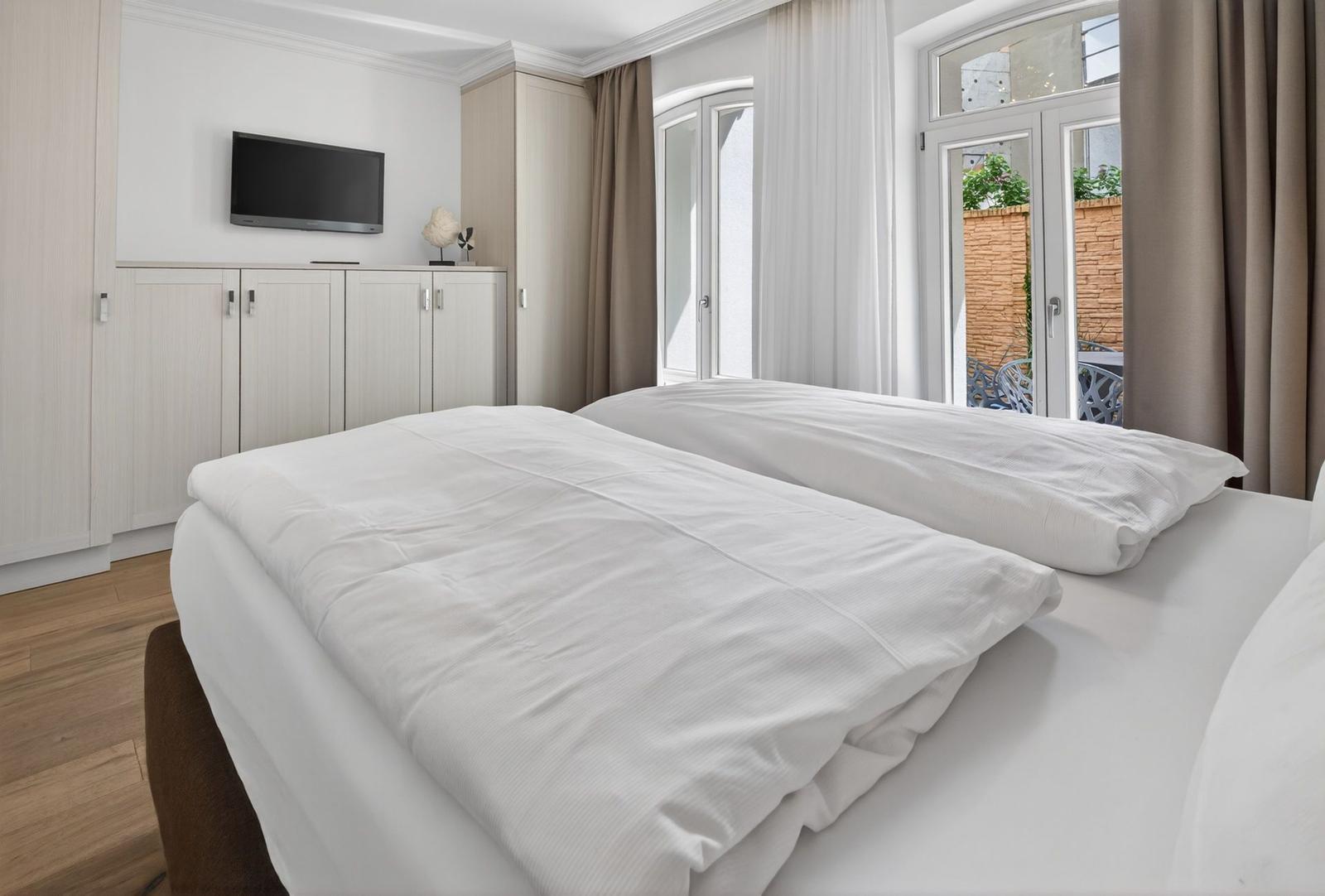 Ein Schlafzimmer mit Doppelbett, TV und Blick auf einen Balkon.
