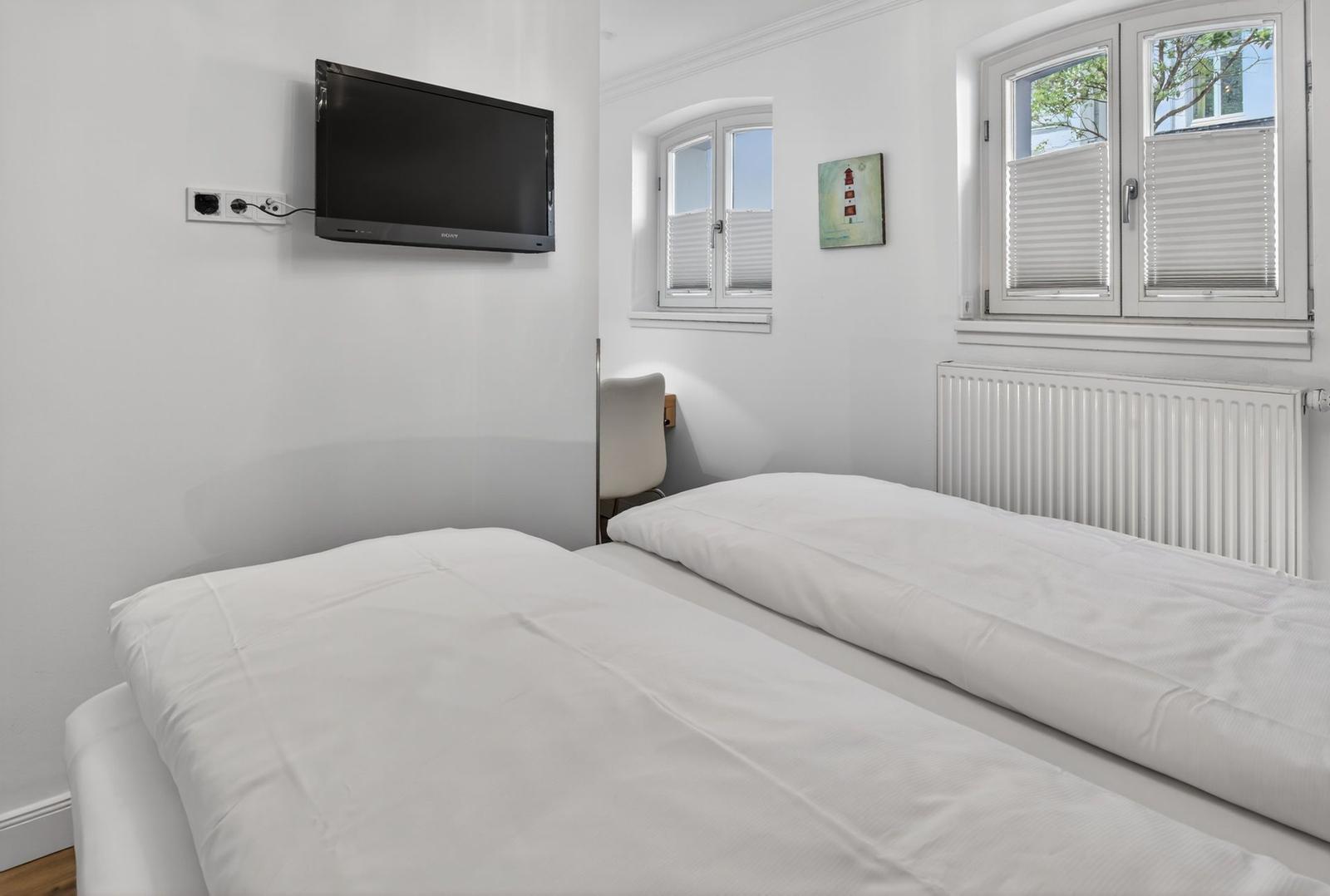 Zimmer mit zwei Betten, Wand-TV und Fenstern mit Jalousien.