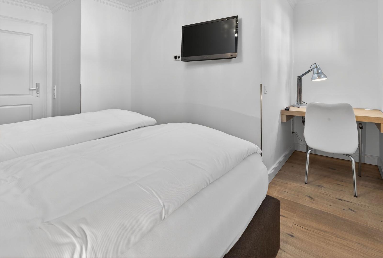 Schlafzimmer mit Bett, Schreibtisch und Wandfernseher.