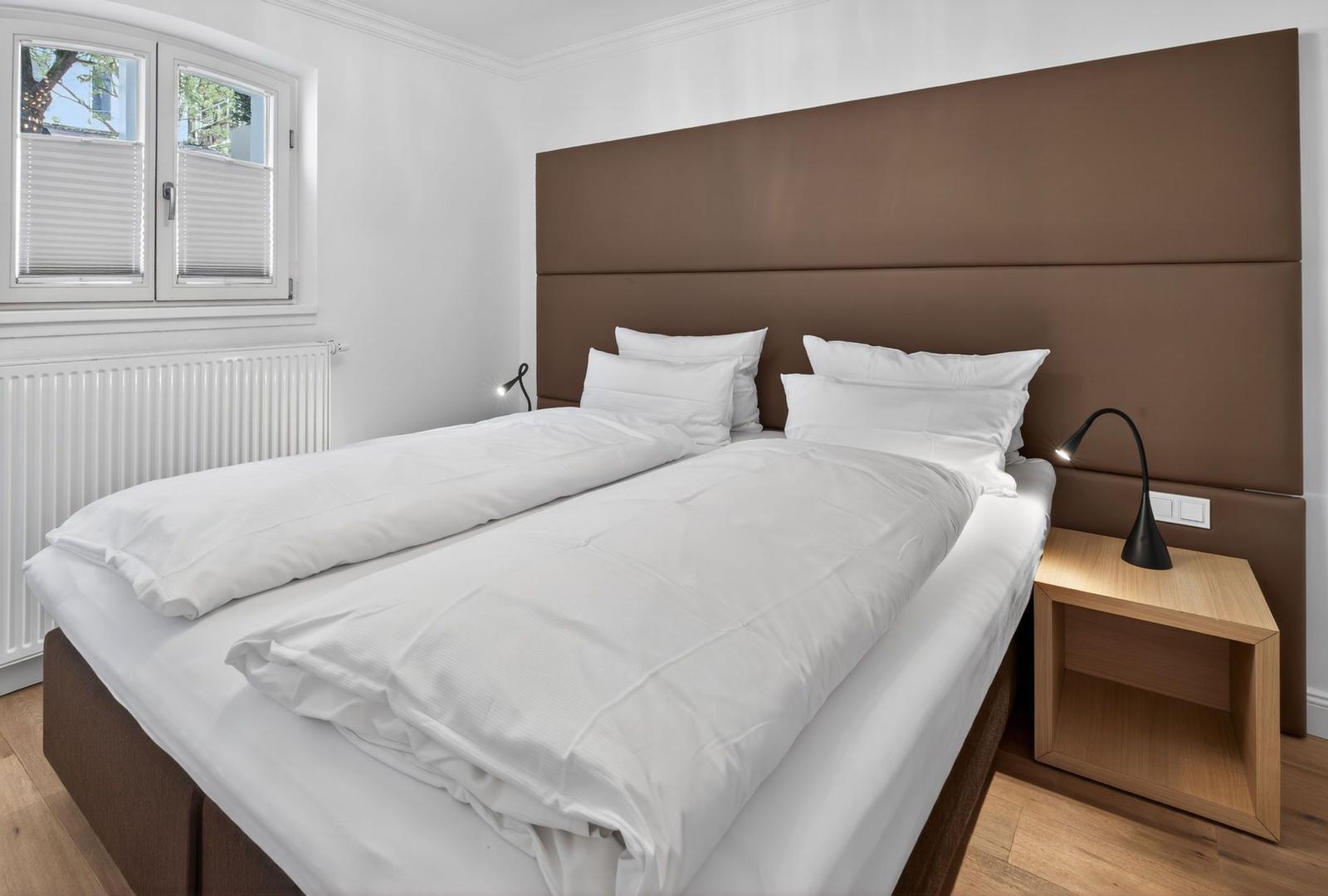Schlafzimmer mit Bett, Nachttisch und Fenster.