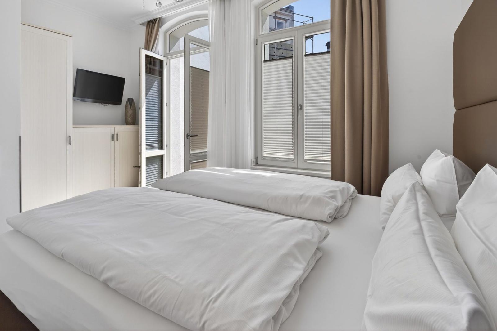 Schlafzimmer mit Bett, Fenstern und TV.