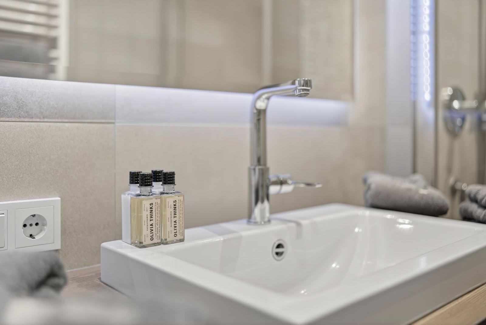 Waschbecken mit modernem Wasserhahn und Flaschen für Pflegeprodukte.