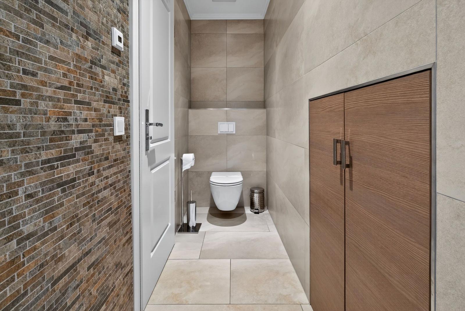 Toilettenbereich mit Steinwand, Toilette, Mülleimer und Holzschrank.