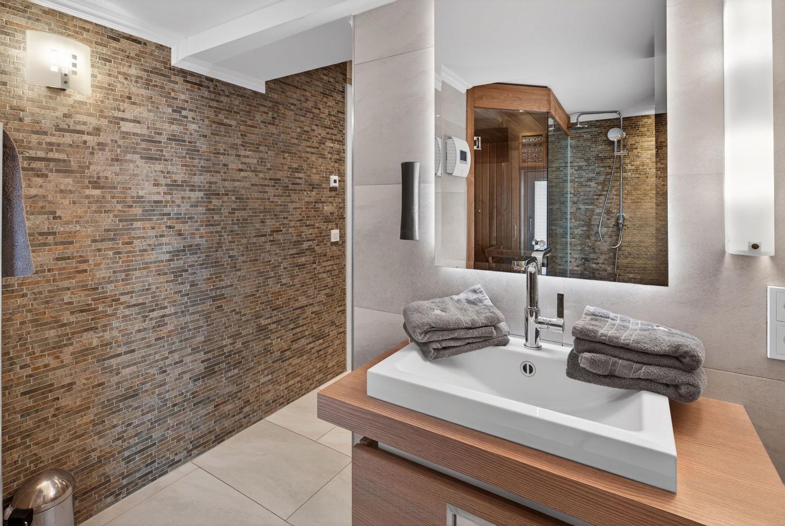 Badezimmer mit Waschbecken, Spiegel und Dusche. Wand aus Steinplatten.