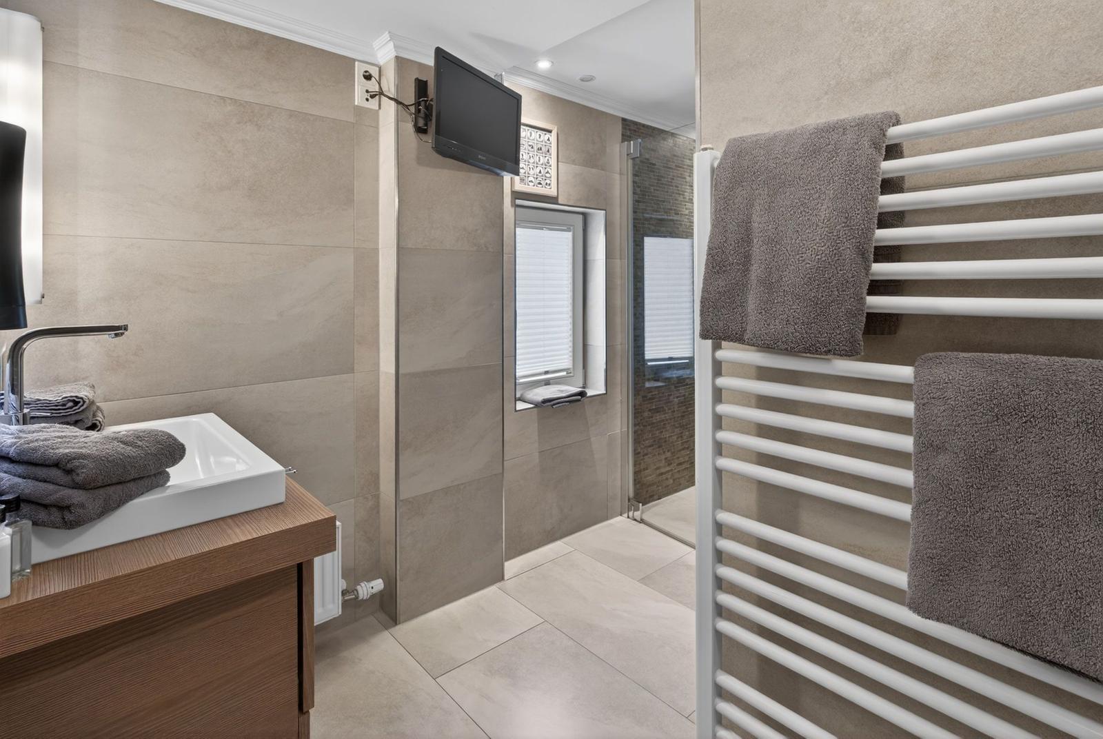 Badezimmer mit Dusche, Waschbecken und Heizkörper für Handtücher.