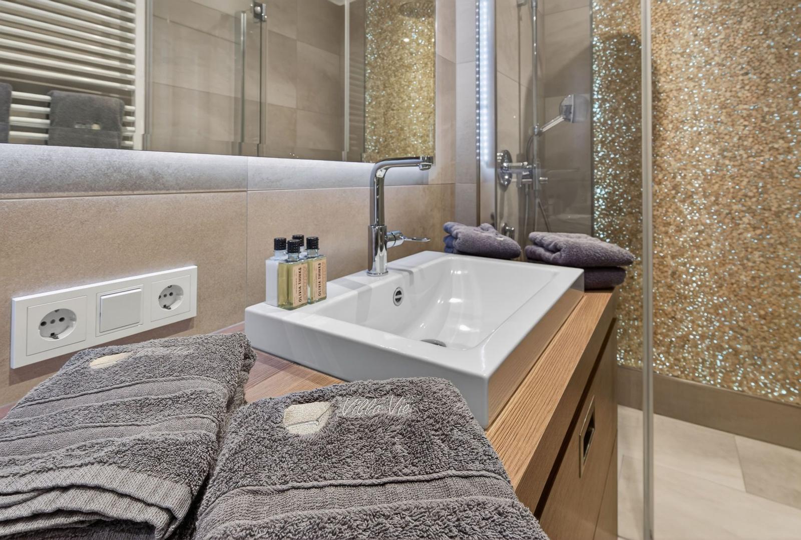 Badezimmer mit Waschbecken, Spiegel, Dusche und Handtüchern.