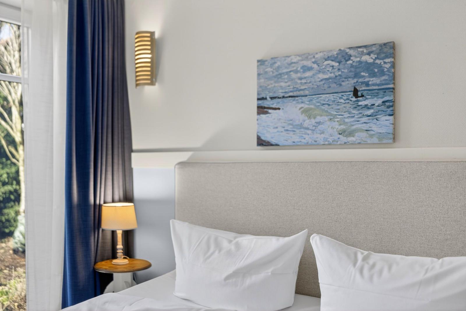 Ein Bett mit weißen Kissen, Wandbild und Nachttisch mit Lampe.