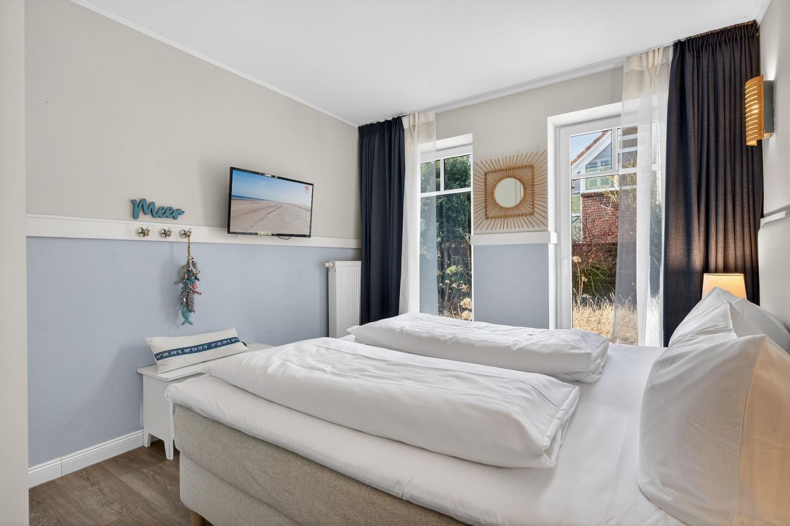 Schlafzimmer mit Doppelbett, TV und Fenster mit Blick auf Außenbereich.