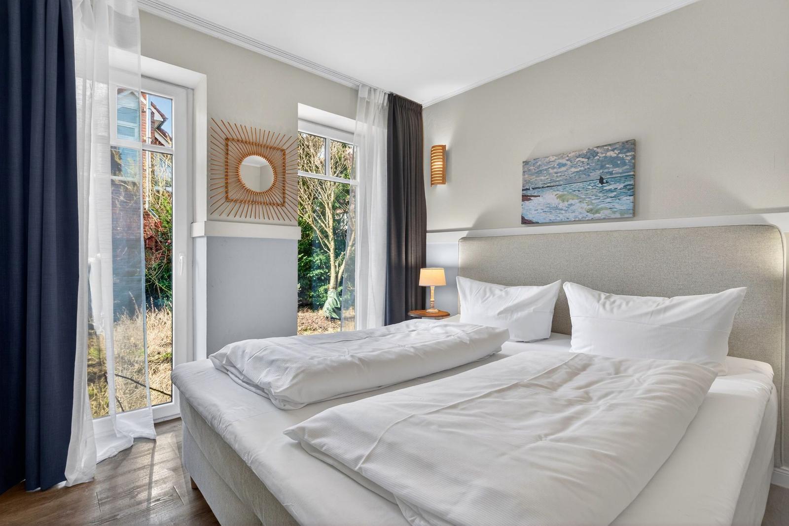 Schlafzimmer mit Doppelbett, Fenstern und Wandbild.