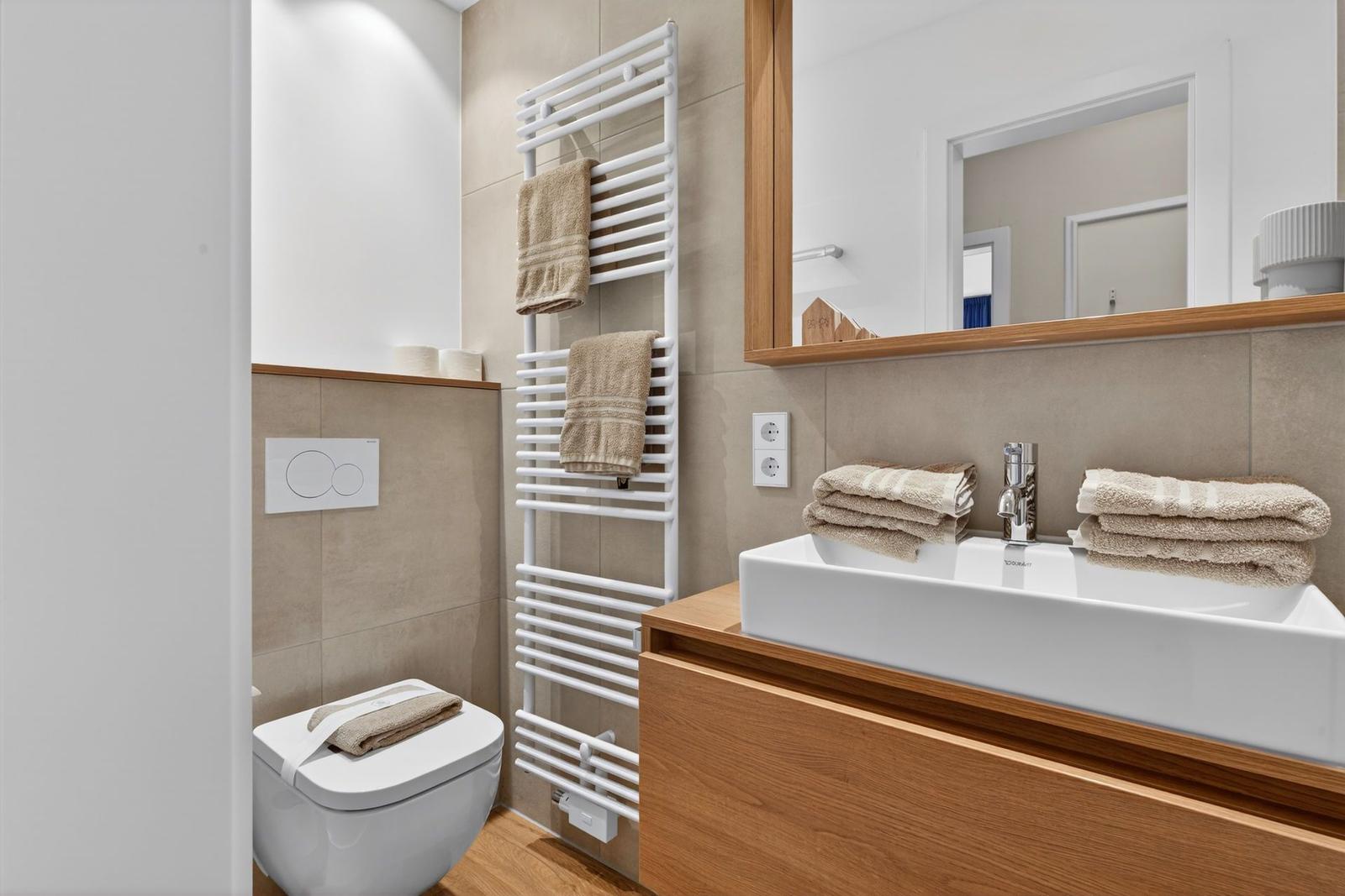 Badezimmer mit Waschbecken, Spiegel, Heizkörper und Toilette. Holz- und Steinausstattung.