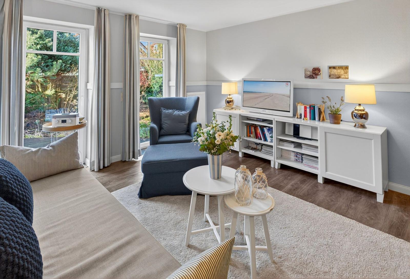 Wohnzimmer mit Sessel, Fernseher und Fenstern zum Garten.