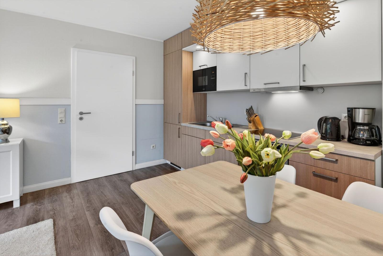 Küche und Essbereich mit Holztisch, Blumen und moderner Beleuchtung.