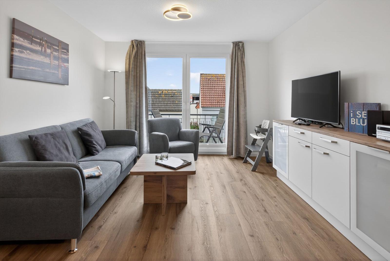 Wohnzimmer mit Sofa, Couchtisch und TV. Balkon mit Sicht auf Dächer.