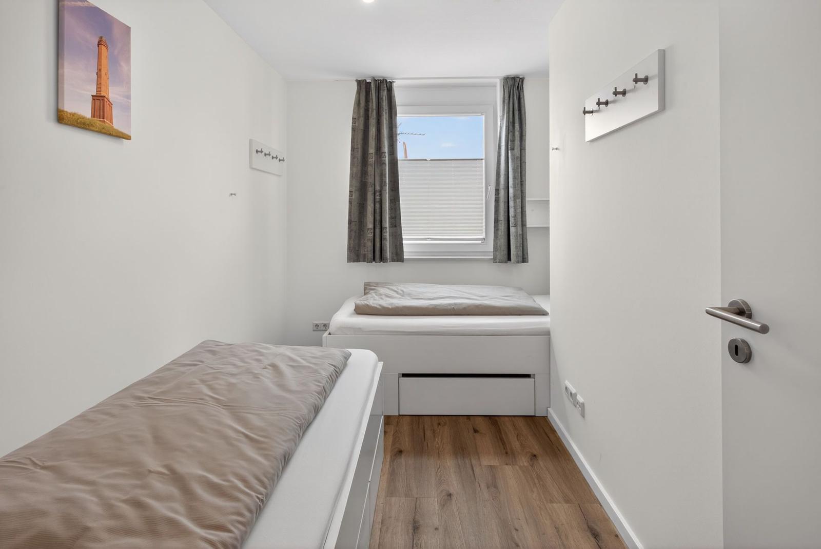 Zwei Betten mit Matratzen und Decken. Holzdielenboden und Fenster mit Jalousie.