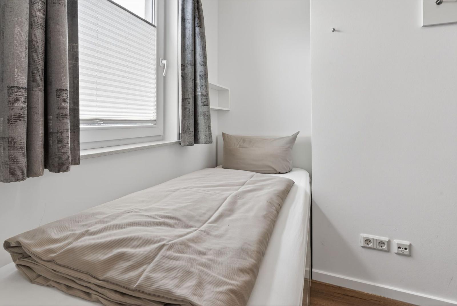 Ein Bett mit Bettwäsche und Kissen unter einem Fenster mit Jalousie und Vorhängen.