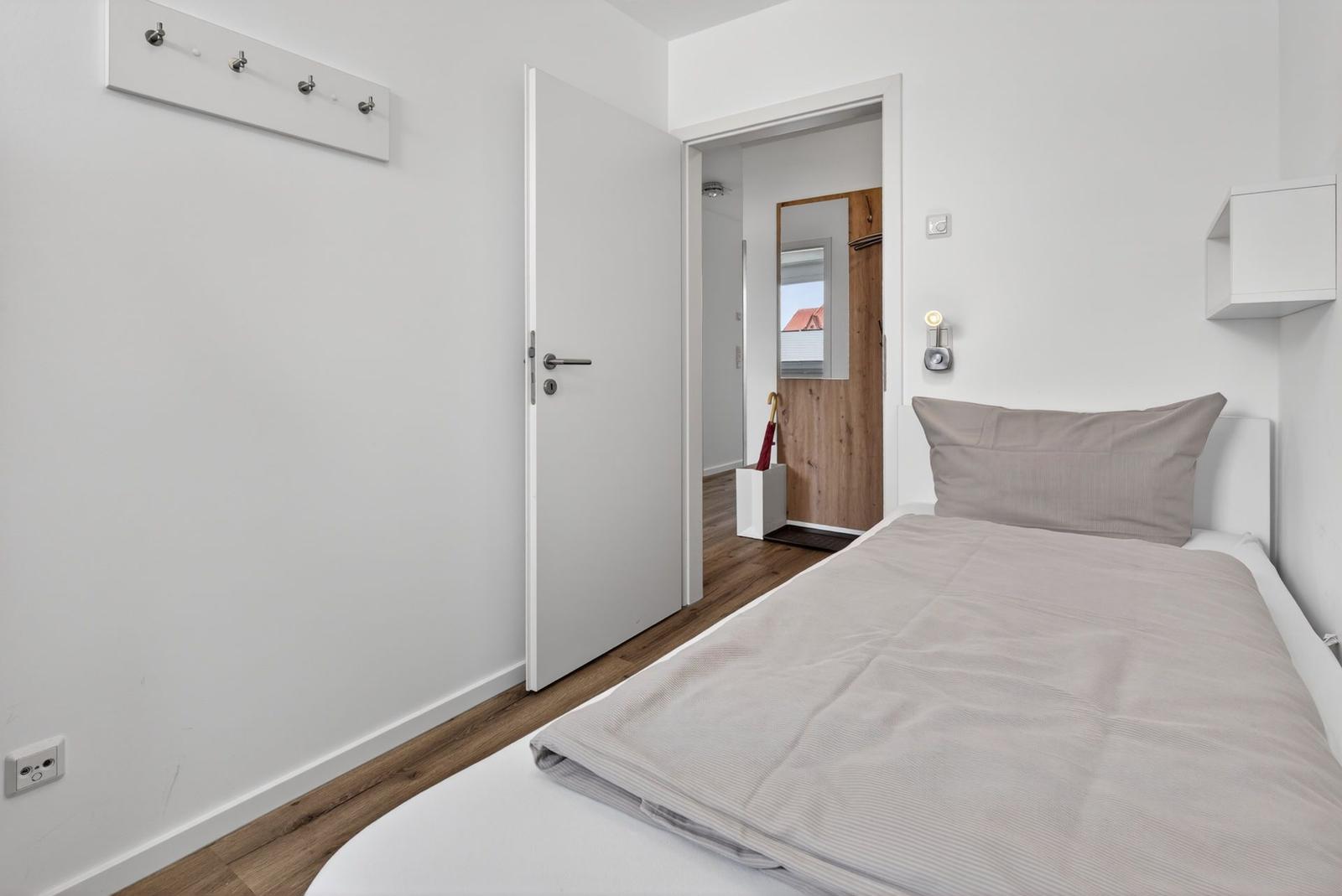Schlafzimmer mit Bett, Wandregal und Tür zum Flur.