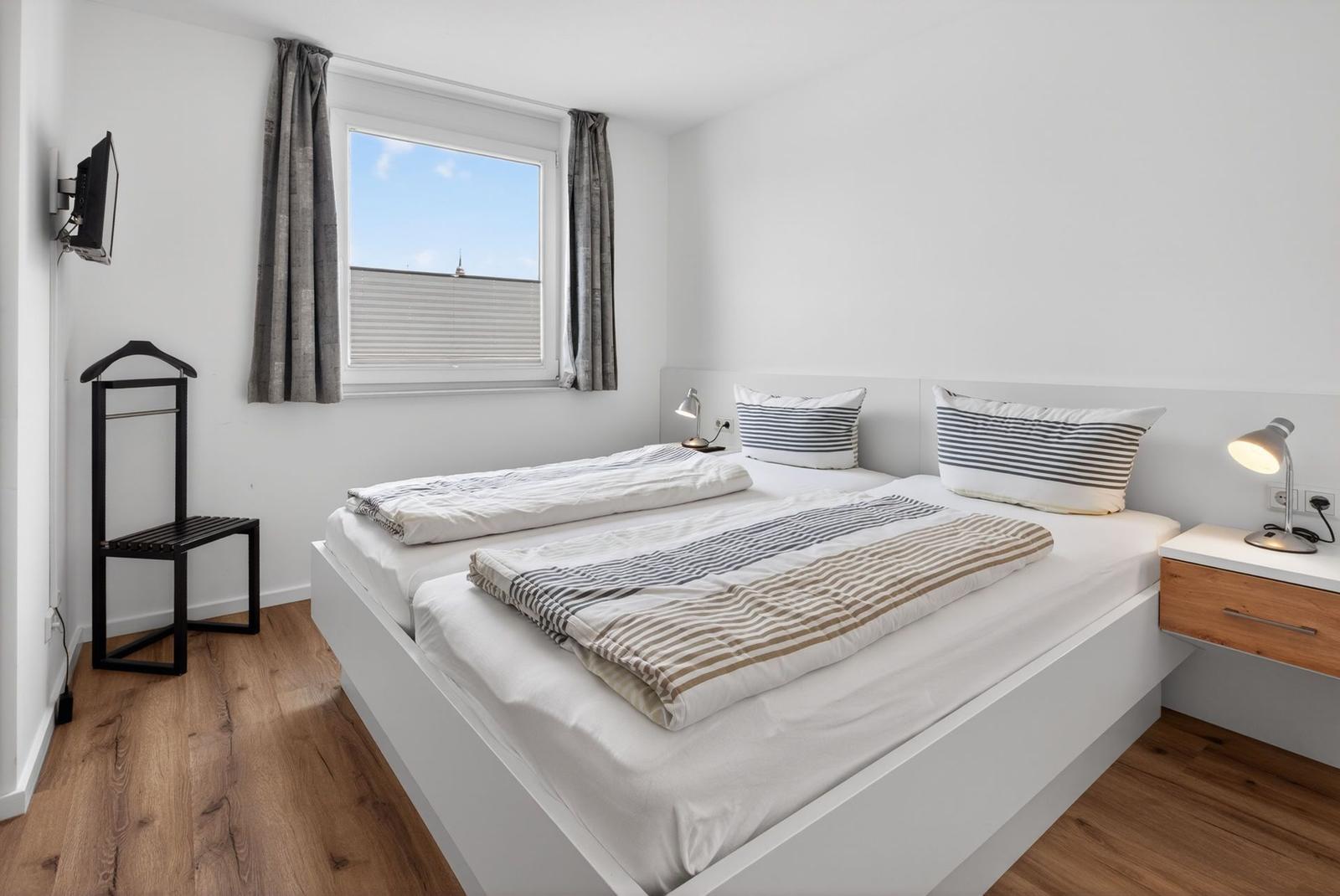 Ein Schlafzimmer mit Doppelbett, Fenster, Nachttisch und Wand-TV.