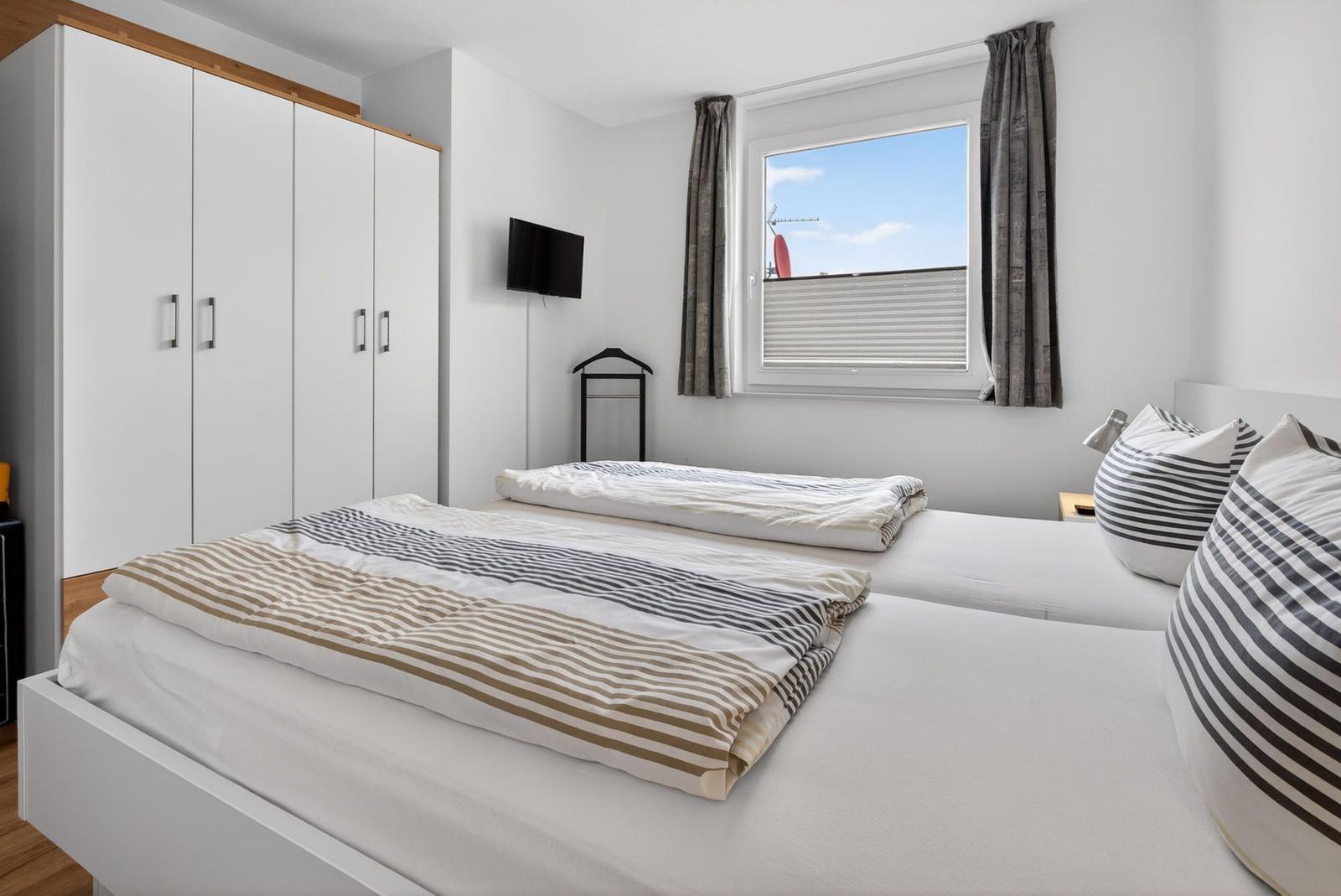 Zwei Betten mit Streifenbetten, Schrank, TV und Fenster mit Blick.