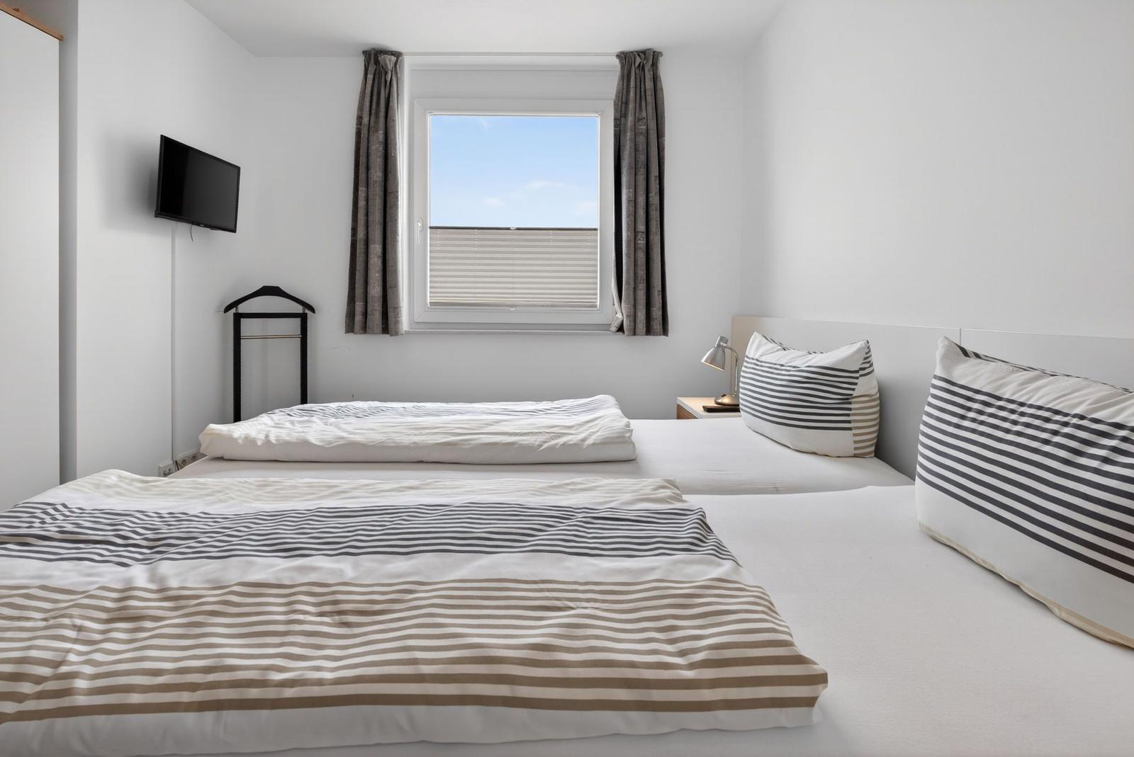 Schlafzimmer mit Doppelbett, Fenster und TV. Bett mit Streifenbezug.