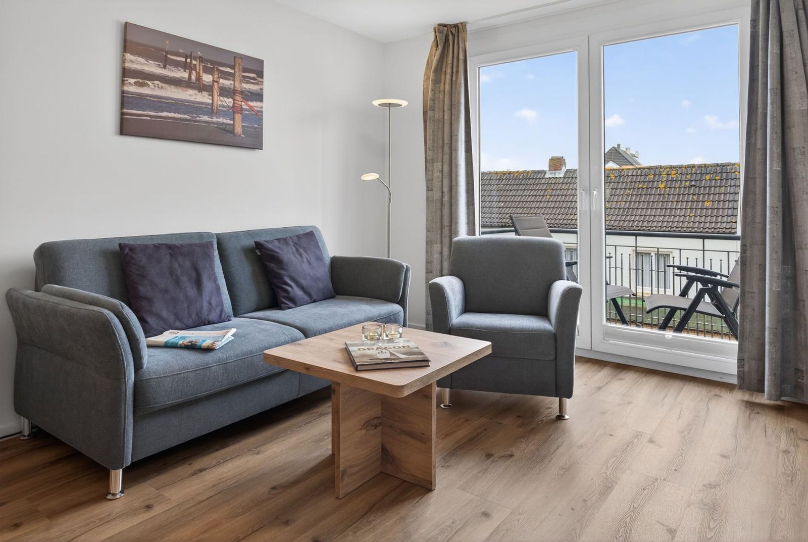Wohnzimmer mit Sofa, Sessel und Tisch. Balkon mit Blick auf Dächer.