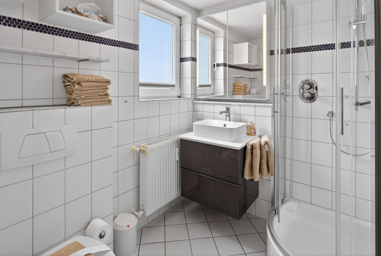 Badezimmer mit Dusche, Waschbecken und Fenster.