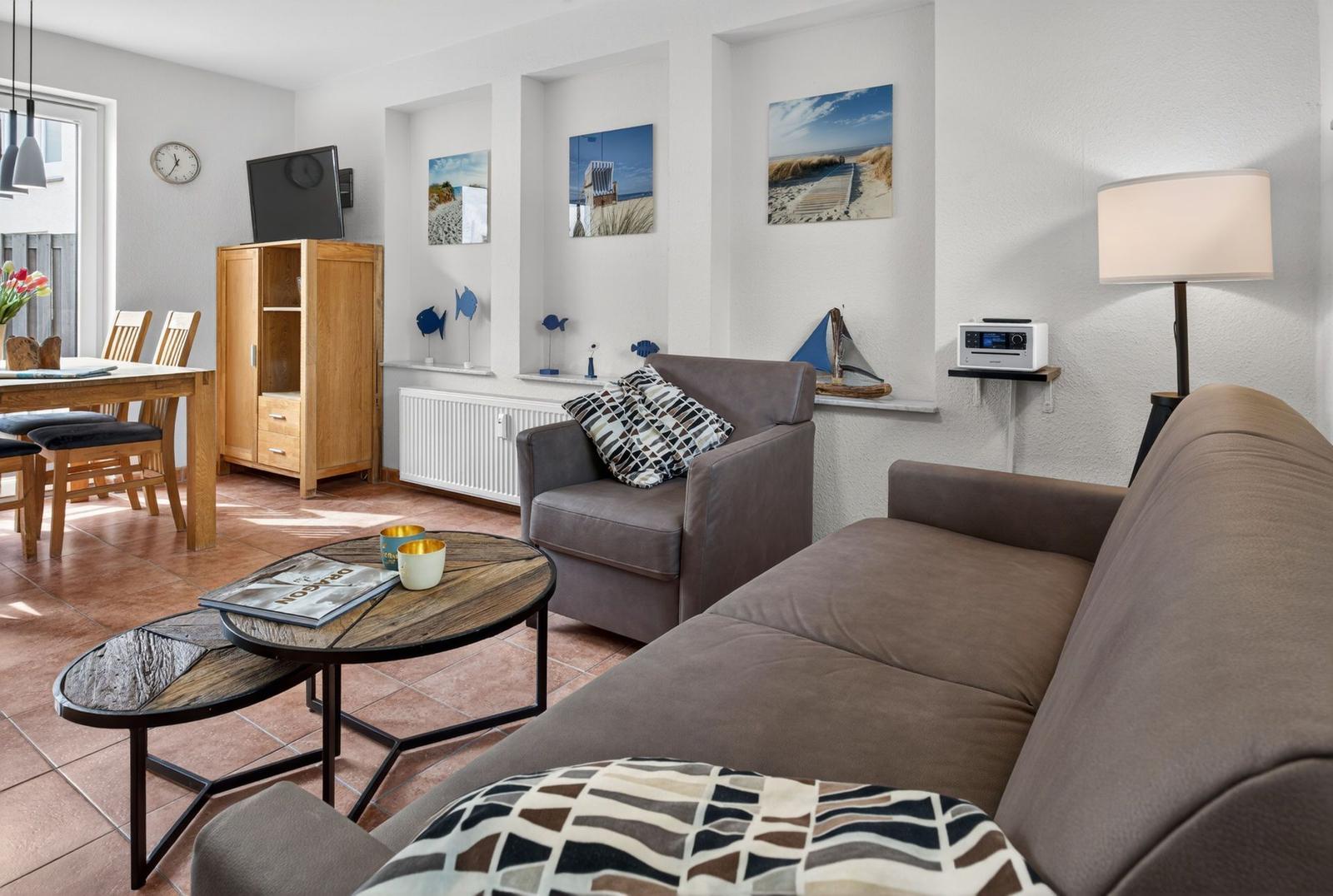 Wohn- und Essbereich mit Sofa, Sessel, Tisch und Wandbildern.