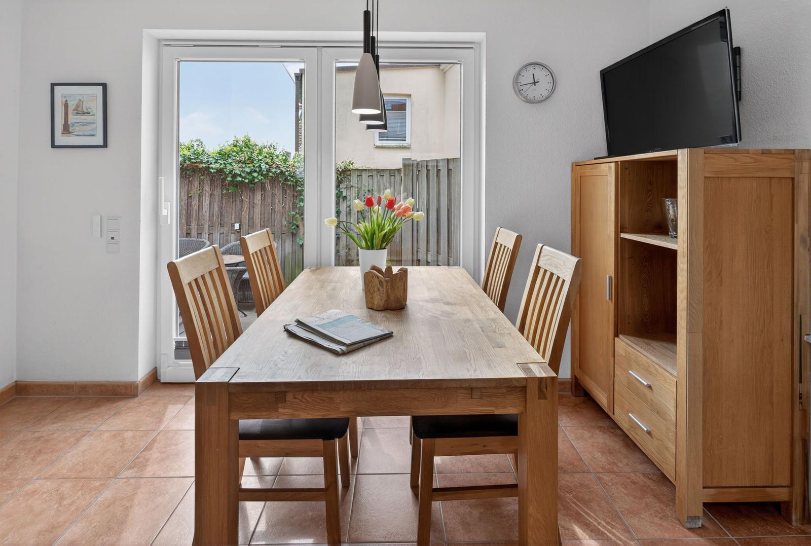 Esszimmer mit Holztisch, Stühlen und Fernseher. Durchgang zur Terrasse mit Garten.