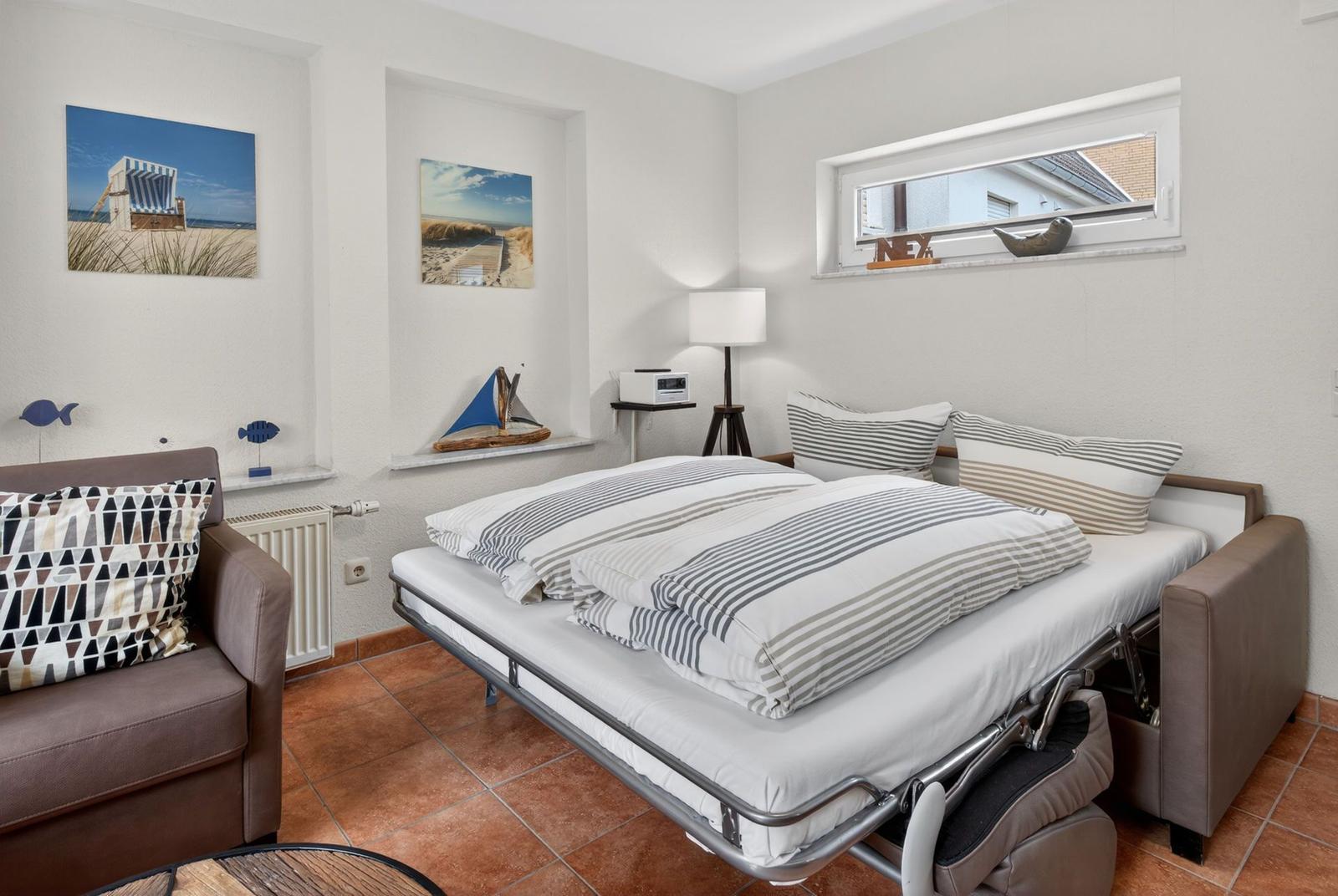 Schlafzimmer mit Bett, Sofa und Wandbildern. Fenster mit Blick auf Dach.