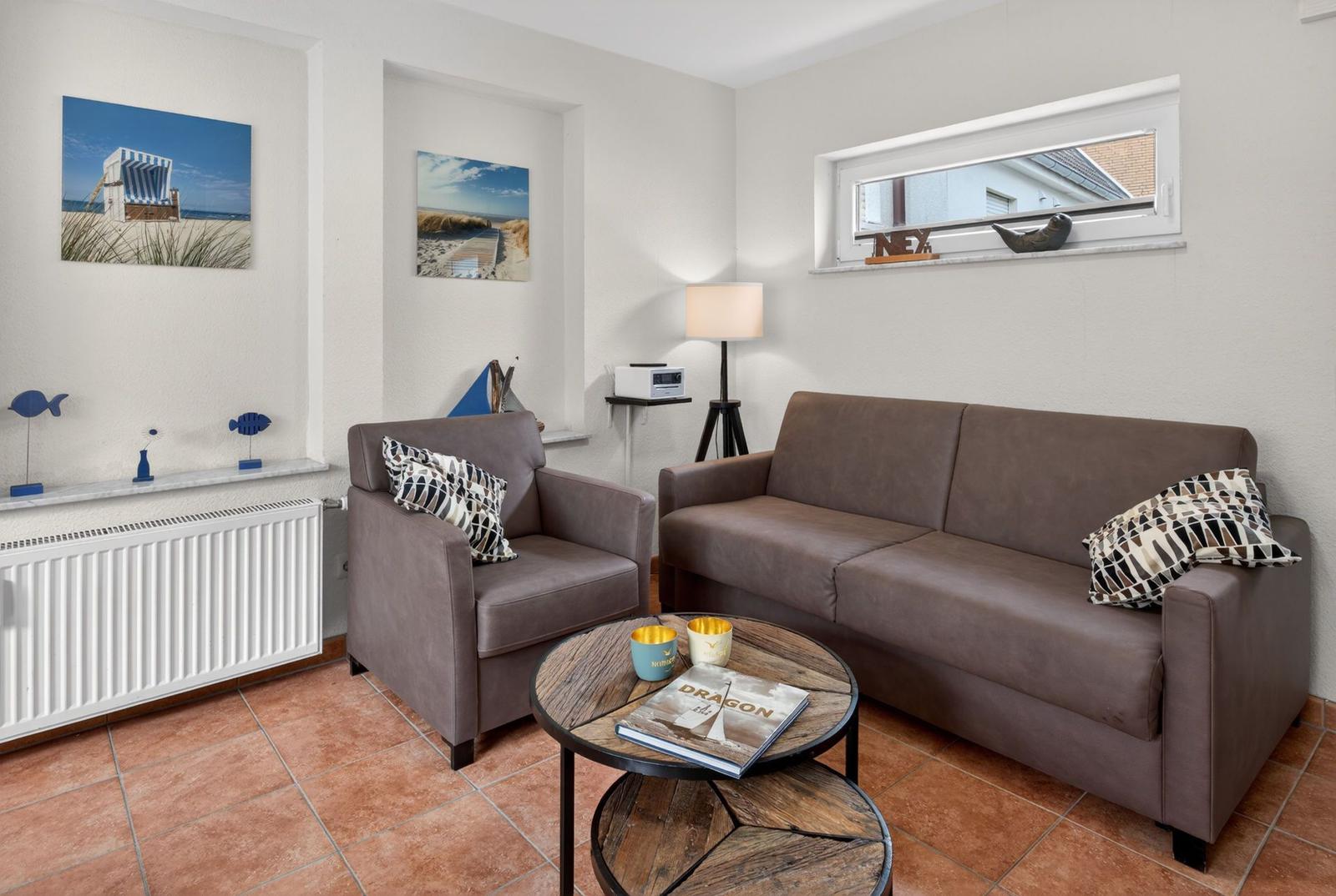 Wohnzimmer mit Sofa, Sessel und runden Tisch. Wandbilder und Fenster mit Blick.