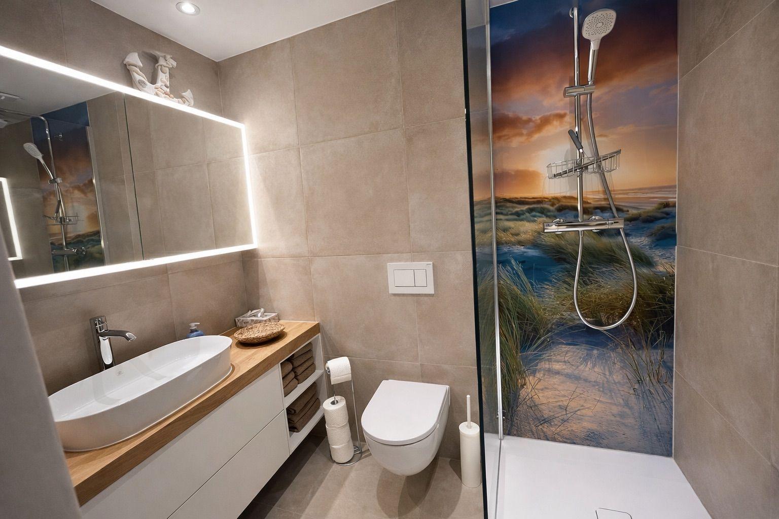 Badezimmer mit Dusche, Waschbecken und Toilette. Duschwand zeigt Strandmotiv.