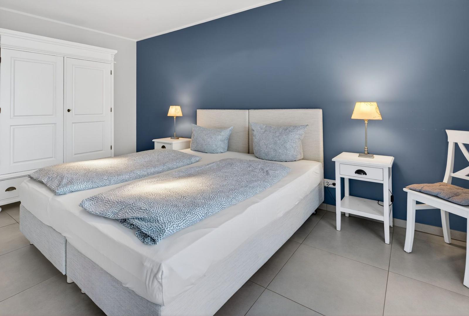 Schlafzimmer mit Doppelbett, zwei Nachttischen und Stuhl an blauer Wand.