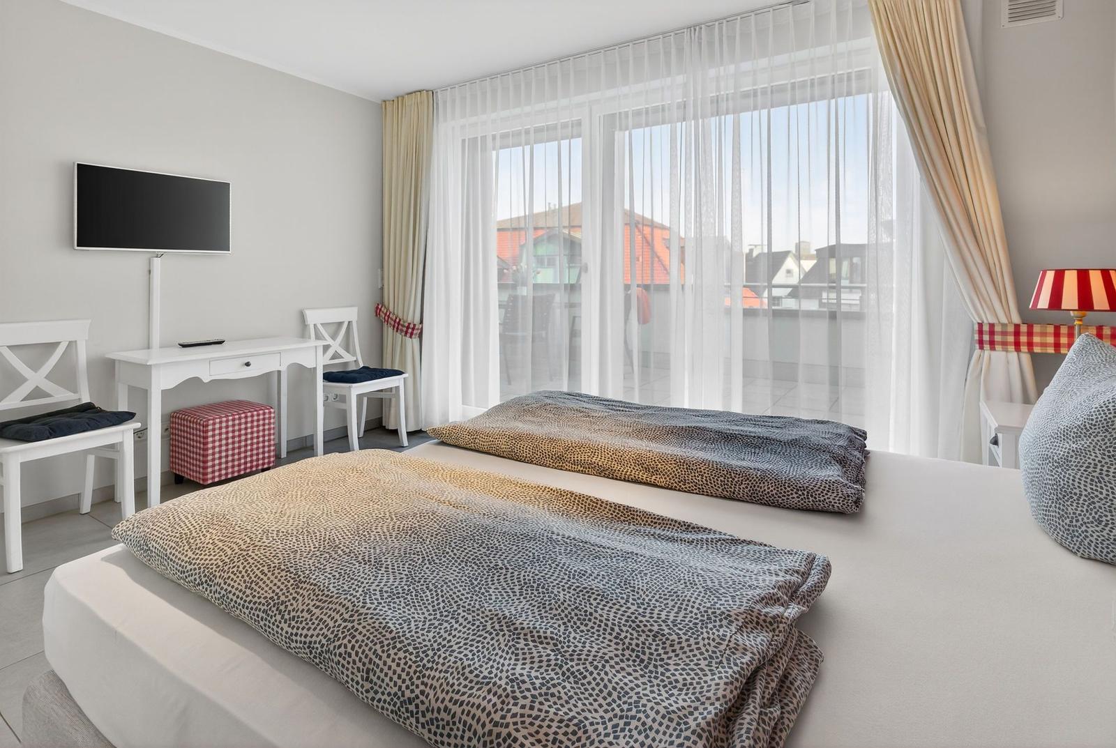 Schlafzimmer mit Bett, Schreibtisch und Blick auf Balkon.