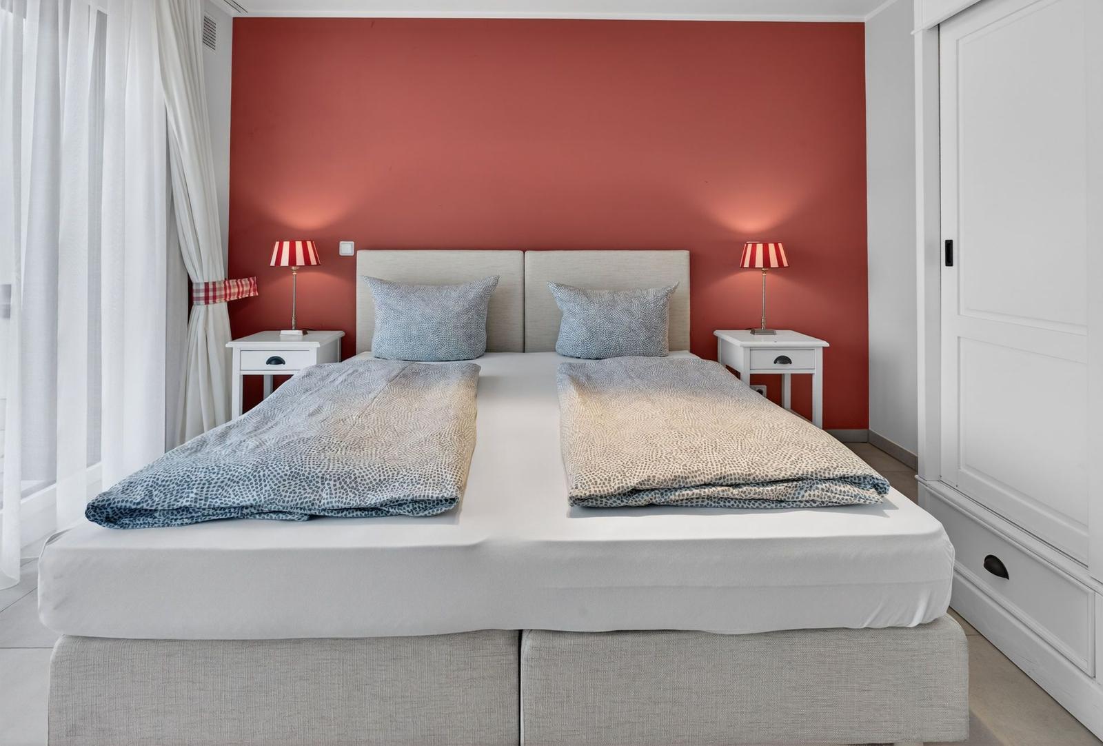 Schlafzimmer mit Doppelbett, roter Wand und zwei Nachttischen mit Lampen.