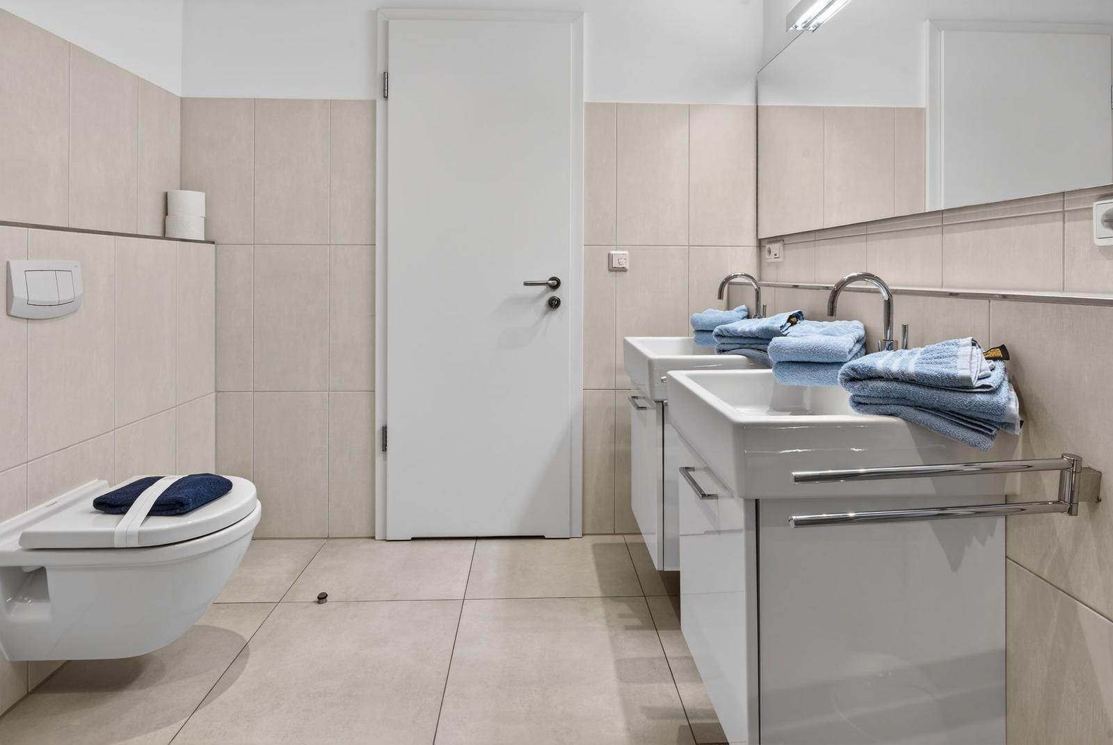 Badezimmer mit Toilette, zwei Waschbecken und Handtüchern.